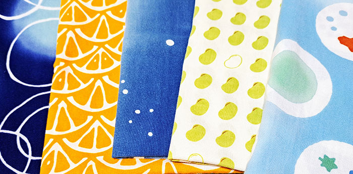 異なるイラストや柄が名入れ印刷された5種類の異なる手ぬぐいが折りたたんだ状態で並んでいる画像