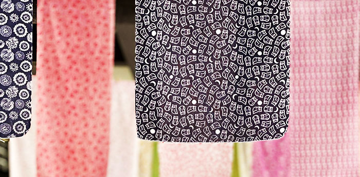 細かい絵柄が全体にプリントされている紺色の手ぬぐいと桃色の手ぬぐいが垂れ下がっているイメージ画像