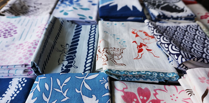 異なるイラスト・柄・模様が名入れプリントされた、複数のオリジナル手ぬぐいが、折りたたんだ状態で並んでいる画像