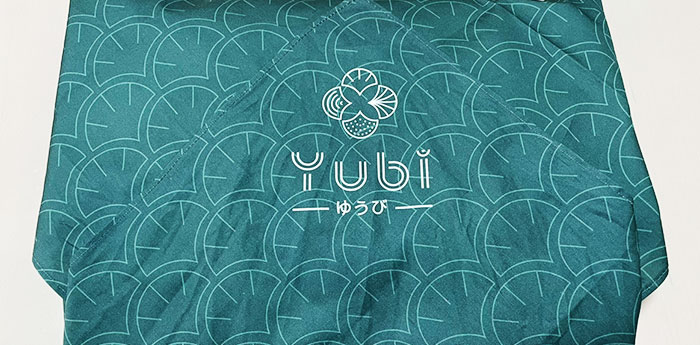 YUbi(ゆうび)というの文字とオリジナルのロゴマークが名入れ印刷された、緑色の生地に模様が入っている風呂敷の画像