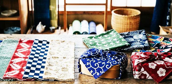 異なるイラストや柄の手ぬぐいと風呂敷が、木製のテーブルの上に並んでいる画像